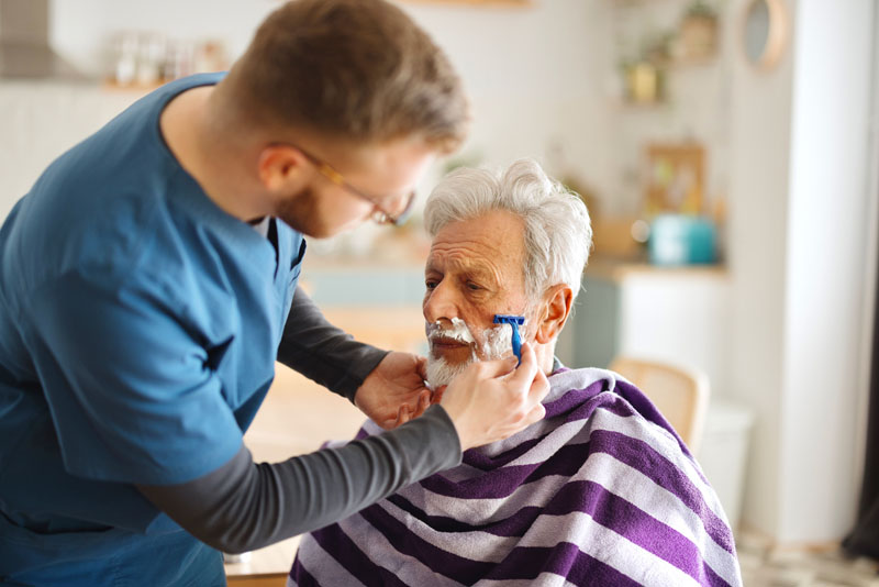 Close up of a caregiver shaving a senior man at home